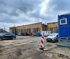 Stara zajezdnia (niski żółty budynek z kilkoma drewnianymi ponumerowanymi bramami wjazdowymi), przed która widoczny jest plac z kostki kamiennej z szynami tramwajowymi, aktualnie zastawiony samochodami. Obszar wymagający rewitalizacji, która zostanie przeprowadzona w ramach Partnerstwa Prywatno-Publicznego.