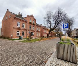 Skrzyżowanie ul. Strajku Dokerów z ulicą Wilków Morskich. Na zdjęciu widoczna ulica z kostki kamiennej, a po lewej stronie odnowione piętrowe budynki z czerwonej cegły.